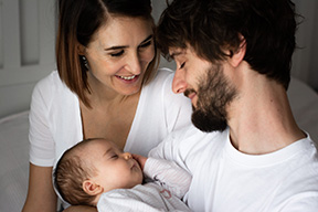 Mama und Papa blicken verliebt auf das schlafende Baby.