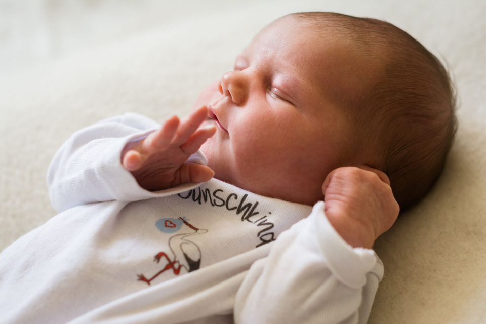 Baby schläft im Strampler mit der Aufschrift Wunschkind.